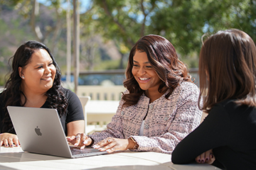 Woman using a laptop with two other women surrounding her