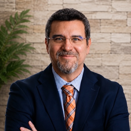 Miguel Gallardo Headshot of Dr. Gallardo in a black suit, light blue shirt, and orange tie