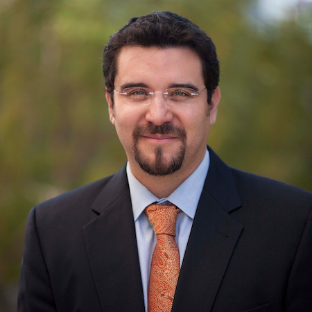 Headshot of Dr. Gallardo in a black suit, light blue shirt, and orange tie