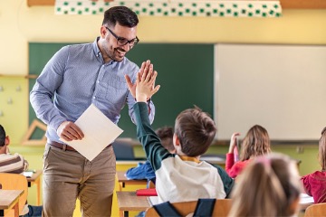 Male teacher high fives young student while passing back papers