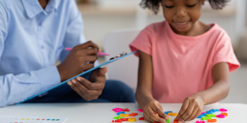 child playing with letters while a therapist watches