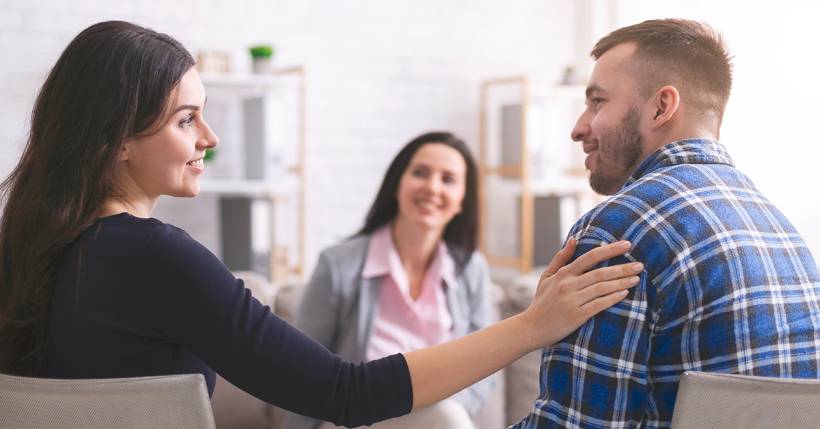 Couple looking at each other sitting with their therapist