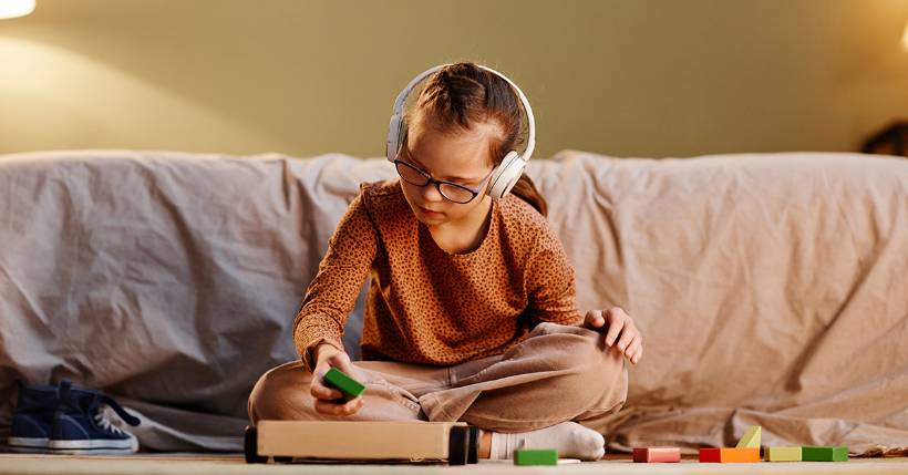 Young girl wearing glasses and over the ear headphones with block in hand