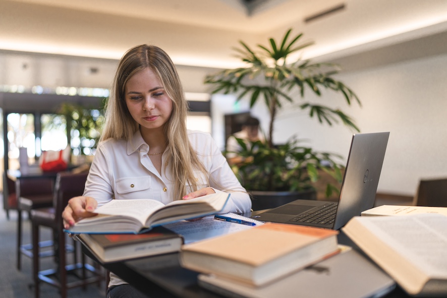 doctoral student sitting on a table with books and a laptop researching global dissertation topics