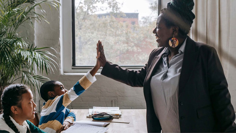 A teachers high-fives her students at their desk.