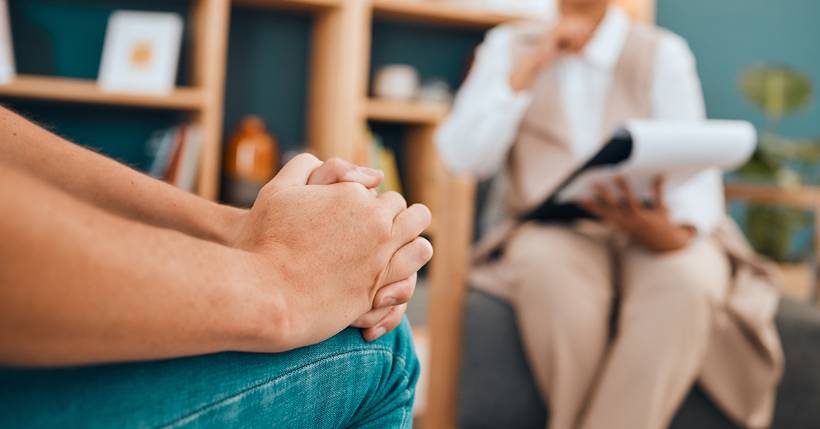 Person sitting with their hands folded on their lap, speaking with their therapist