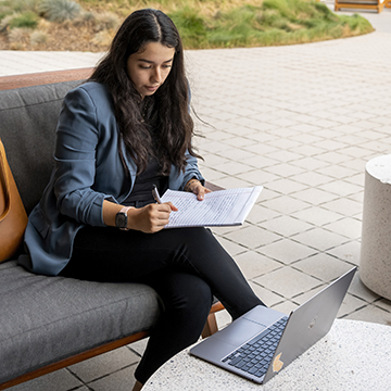 Young woman taking notes while looking at her laptop