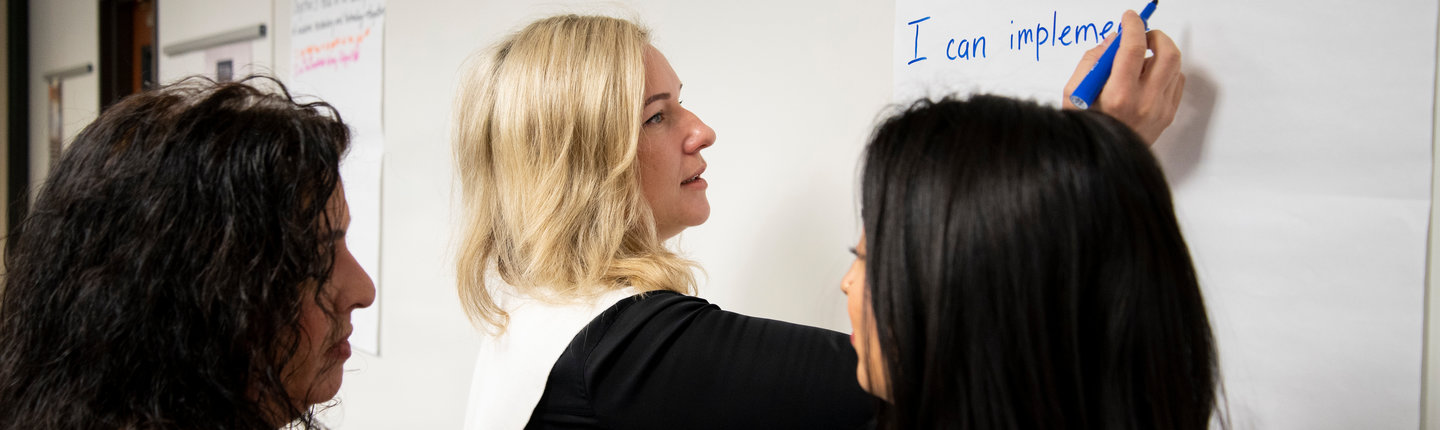 blonde woman writing on a whiteboard 