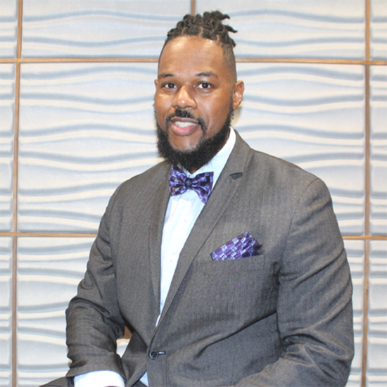 Dr. Erlanger Turner sitting for headshot in a grey suit with purple bowtie